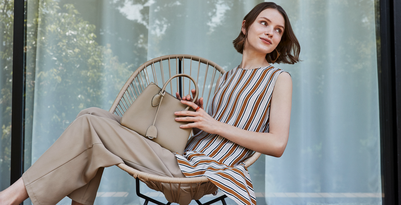 An elegant woman happily holds a luxurious bag made of high-quality full-grain leather.