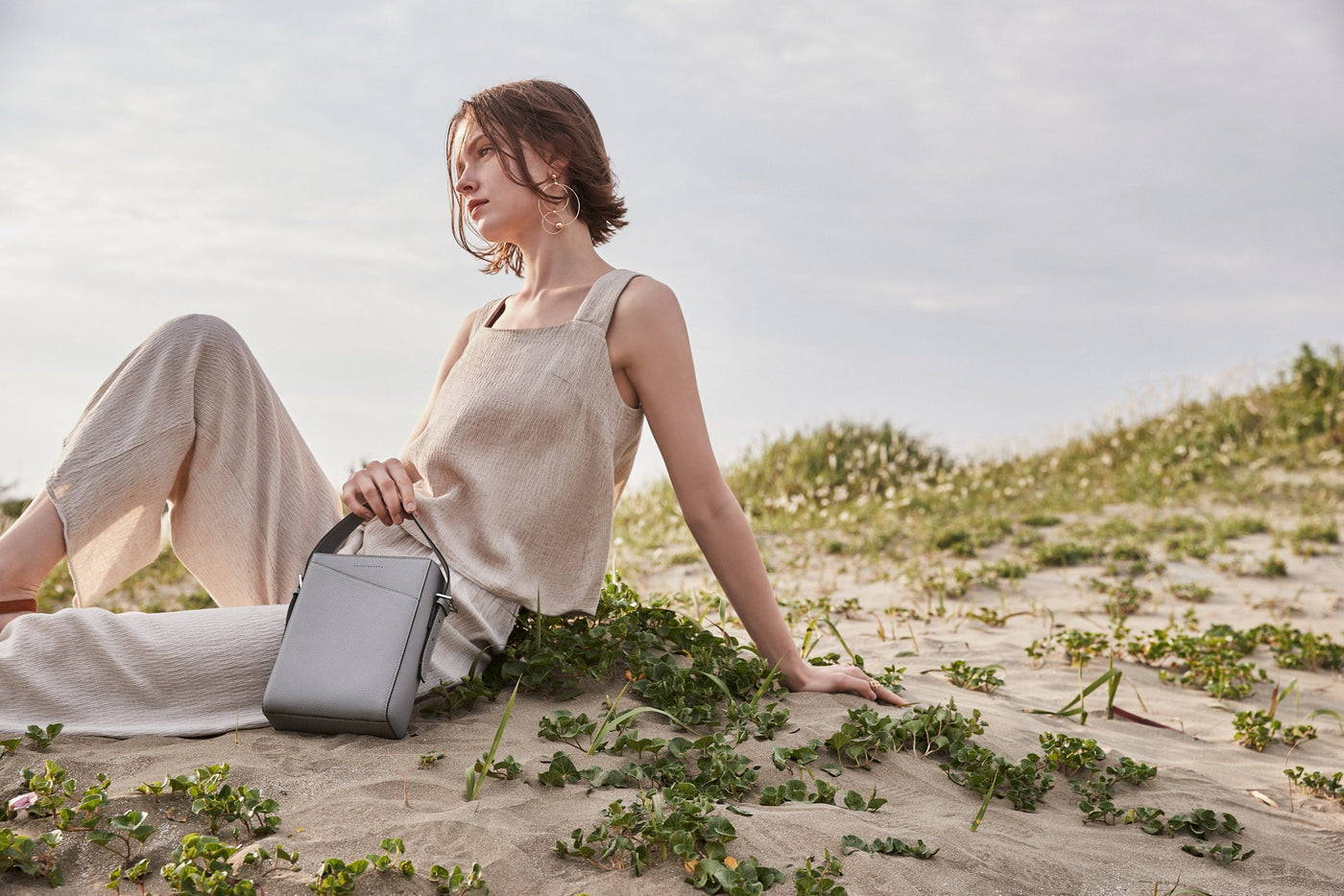 A stylishly dressed, environmentally conscious woman carries a sustainable leather bag from BONAVENTURA on the beach.