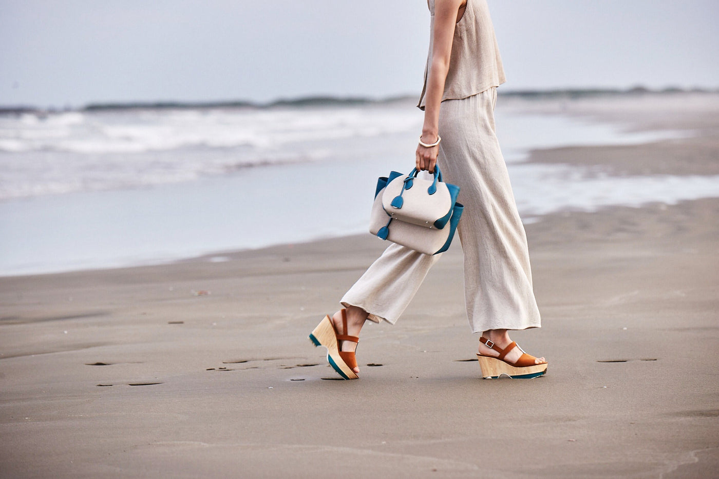Woman with an elegant beach bag walks on a sunny beach.